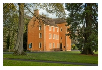 Pittencrief House, historic three-storey building sandwiched between two trees. The building is a reddish-orange colour, which contrasts with the green of the trees and surrounding grass.