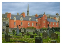 In the foreground is an old graveyard with a wall at the rear. Behind the wall is the rear view of the historic Abbot House, a red coloured stone building.