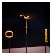 A gold bird on a long pin, a gold ring and a cigar shaped gold ingot